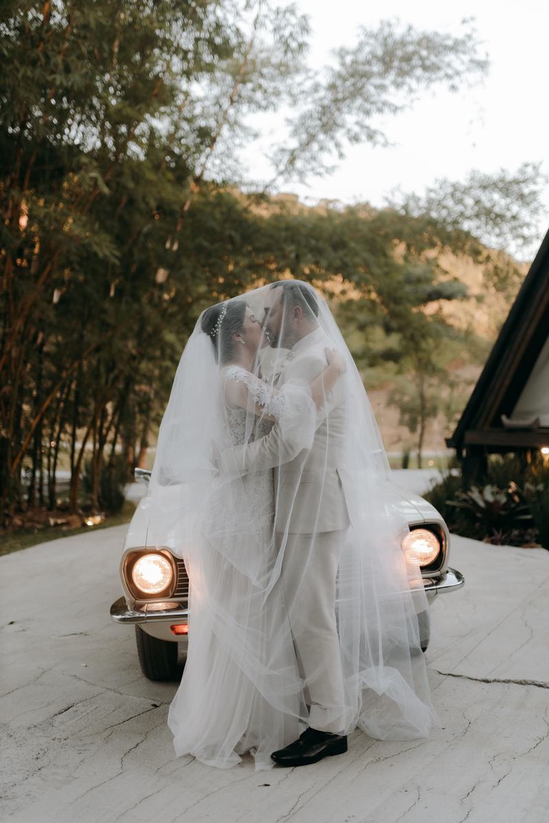Bride under a veil beside a vintage car