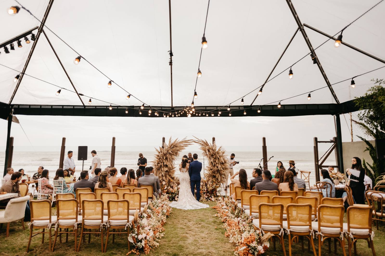 Beach wedding ceremony under string lights with a floral arch